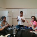 A professor, three students, and an Undergraduate Teaching Assistant practice using pipettes.