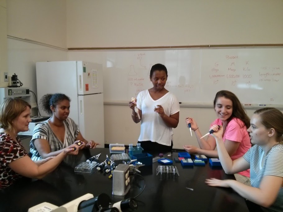 A professor, three students, and an Undergraduate Teaching Assistant practice using pipettes.